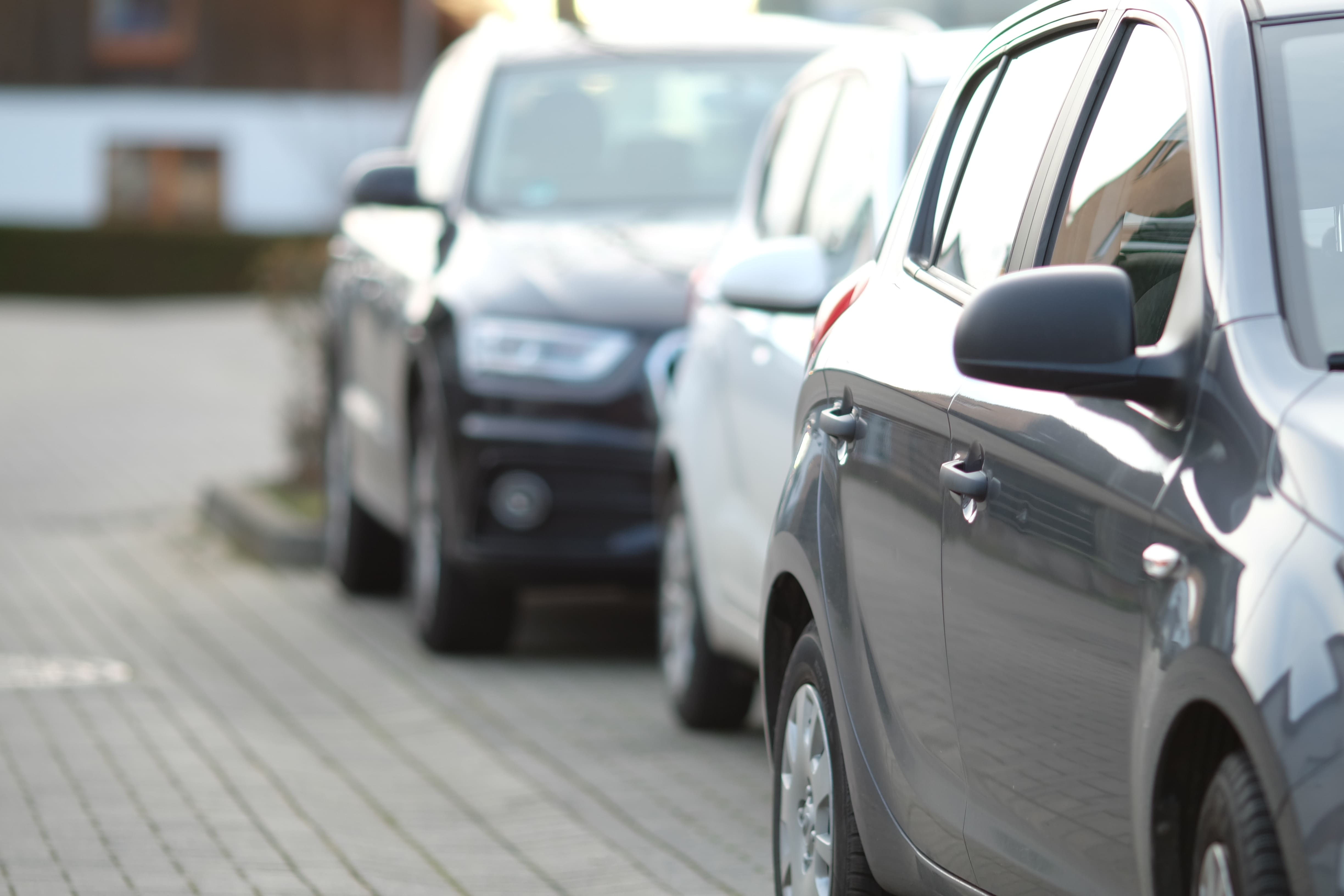 Fileira de carros estacionados paralelamente em uma rua pavimentada com blocos de concreto.